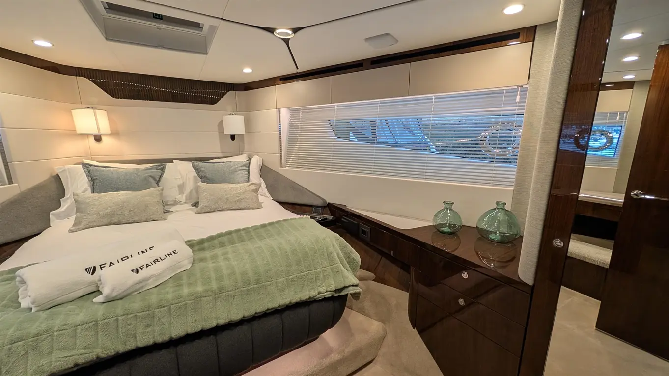 Luxury yacht bedroom featuring a double bed, soft blankets, stylish decor, and light flooding through Venetian blinds.